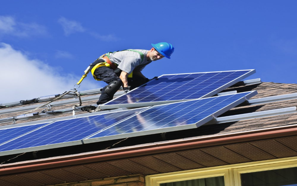 A man wearing safety gear while mounting solar panels on a roof.